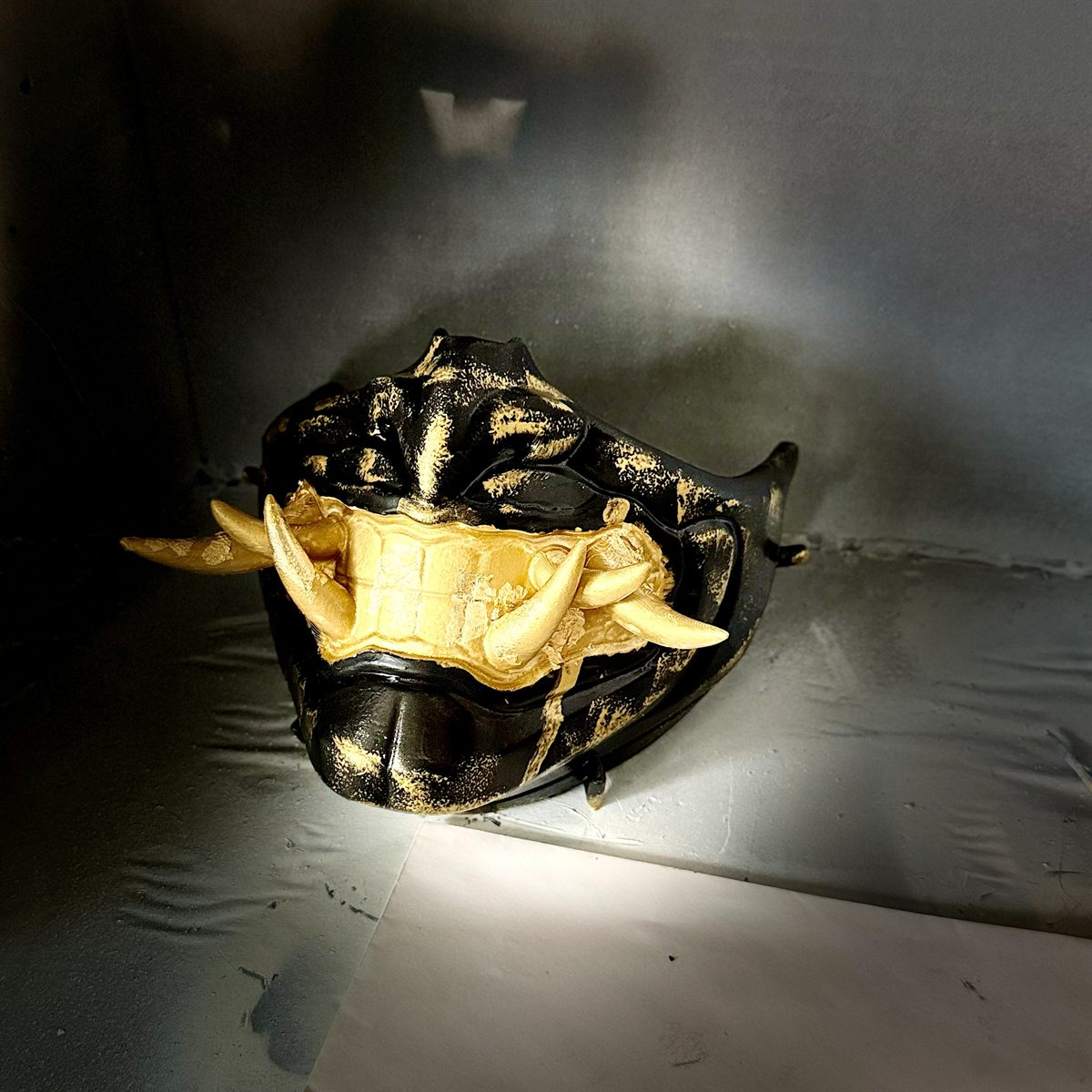 Black and gold oni mask under dramatic lighting
