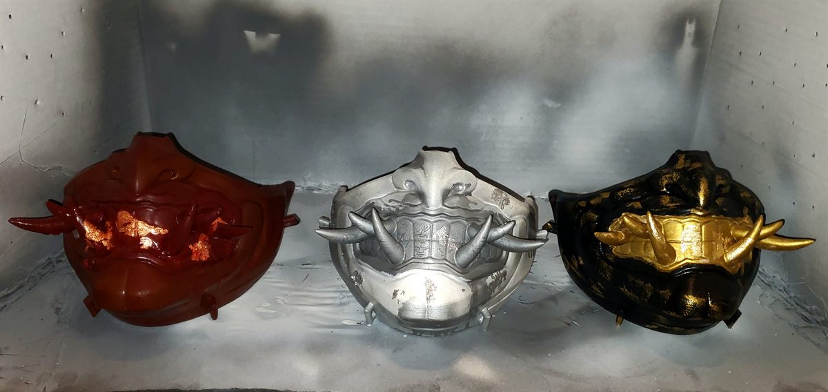 Three painted oni masks in red, silver, and black and gold
